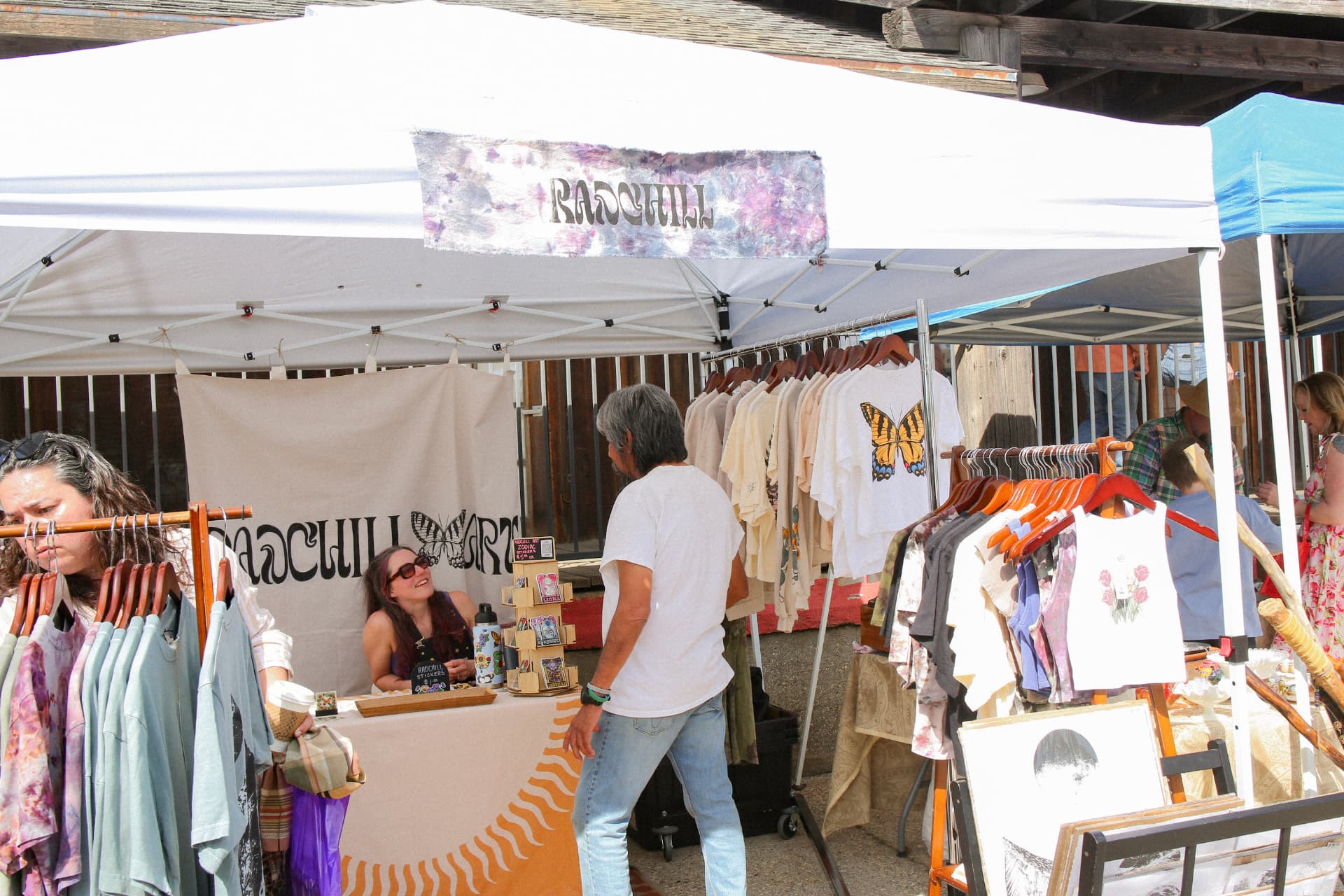 A maker's clothing booth with hand-printed tees and tie-dye under a white canopy.